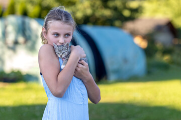Young cheerful smiling girl playing with domestic kitten. Woman on farm rejoicing at birth of pet. Child playing with cat in yard of family house or park