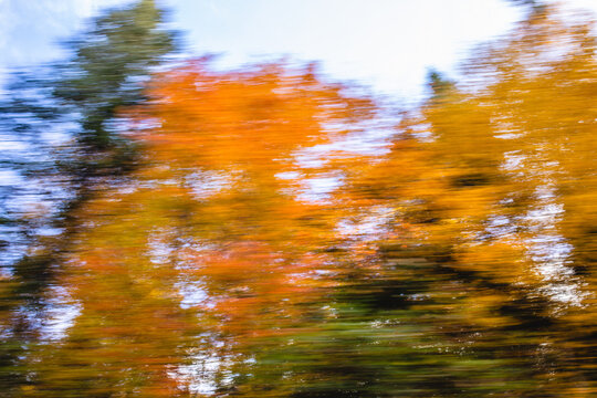 Colorful autumn leaves blur as a vehicle moves quickly through a scenic landscape in fall season