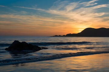 Fototapeta premium Dramatic sunset over a rocky coastline with waves gently lapping the shore