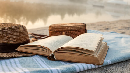 Relaxing beach scene with a book, hat, and picnic basket.
