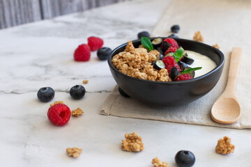 Healthy breakfast bowl with granola, yogurt, raspberries, blueberries, and mint on a linen napkin. 