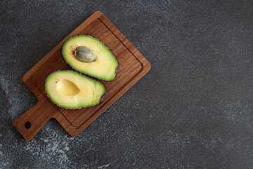 Avocado halves on a wooden cutting board, placed on a dark textured background. 