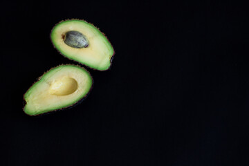 Avocado halves on a dark black background, arranged in the corner of the frame. Minimalist food composition, top view.