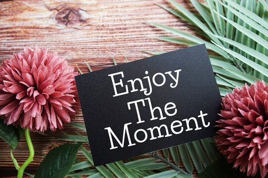 Naklejki Enjoy The Moment Motivational and Inspirational quotes with flowers bouquet decoration on wooen background