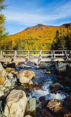Autumn bridge crossing over a clear mountain stream amidst vibrant fall foliage in a scenic landscape