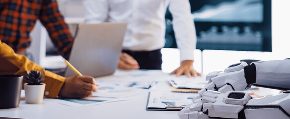 Professionals engage in a collaborative meeting with a humanoid robot, analyzing financial charts and data in a sleek, modern office setting.Noogenesis