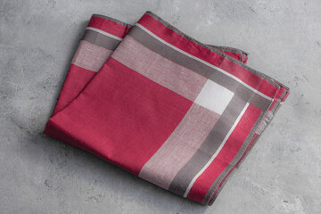 A single, neatly folded plaid handkerchief with a bold red pattern and gray accents rests on a textured gray background.