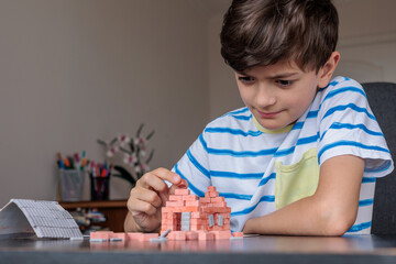 young boy at home builds a miniature house from toy ceramic bricks, focusing on construction and creativity. logic, fine motor skills, and concentration. autism support, ADHD therapy, screen free  © Светлана Мищенко