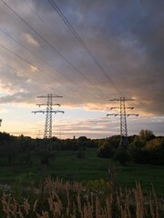 High-voltage tower among trees and clouds in evening sky