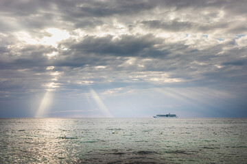 Cruise ship sailing through calm waters under dramatic clouds and sunlight rays at midday on the ocean