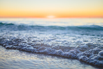 Ocean waves gently lap the shore at sunset with vibrant colors illuminating the sky above