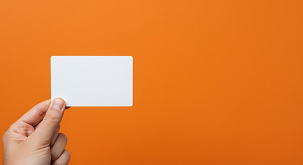Hand Holding Blank White Card Against Vibrant Orange Background: Minimalist Mockup for Design Presentation.