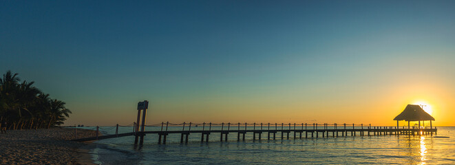 Sunrise over the tranquil pier and sandy beach at a coastal paradise with palm trees in the foreground