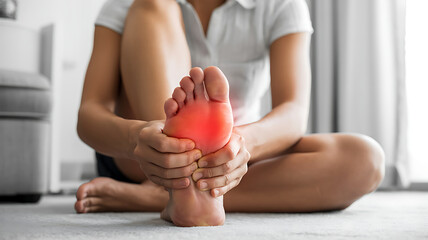 Woman suffering from plantar fasciitis, holding her foot in pain with red spot indicating inflammation medical technology
