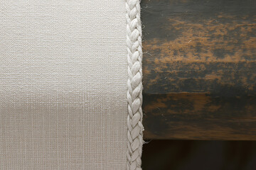 Close up abstract detail of a textured white fabric edge with a braided trim next to a dark textured background creating a subtle contrast