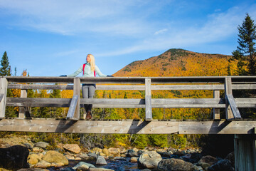 Hiker enjoys scenic view from wooden bridge in autumn landscape near mountain stream