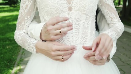 Close-up of intertwined hands of European newlyweds holding wedding rings near their chests. Their fingers interlock in a chess pattern, symbolizing unity, love, and commitment.