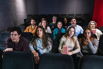 Group of people enjoying a film screening, holding popcorn buckets and experiencing various emotions in a dark theater