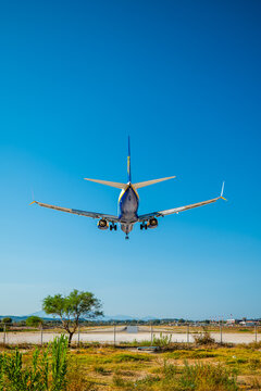 Airplane approaching Zakynthos Airport Greece flying low above runway with landing gear down clear blue sky background and dry grass in foreground