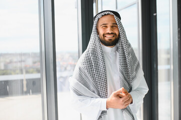 Smiling arab businessman wearing traditional kandura posing in modern office building