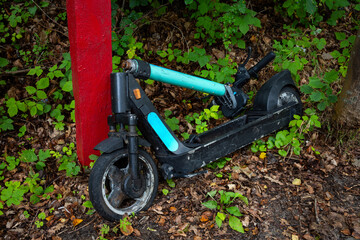 Fototapeta premium A damaged public electric scooter lies on the side of the road. The photo was taken on a cloudy day with natural lighting.