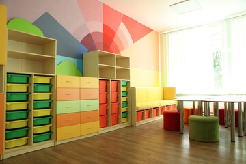 Desks, chairs and shelving unit near bright wall in classroom