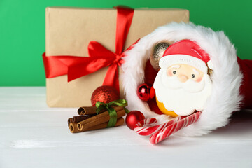 Happy Saint Nicholas day. Baubles, gift box and sweets on white wooden table against green background, closeup