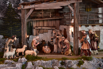 Weihnachtskrippe im alpenl&auml;ndischen, l&auml;ndlichen Stil, mit Bergen und Nachthimmel als Hintergrund, in gem&uuml;tlichem Stall aus alten Holzbalken und stimmungsvoller Beleuchtung
