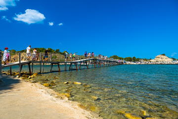 Wooden bridge leading to Cameo Island Zakynthos Greece with clear turquoise water below and tourists walking across popular instagram travel spot
