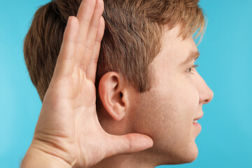 Fototapeta premium Sound. Sound. Man showing hand to ear gesture on light blue background