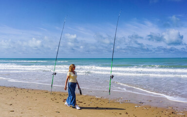 A lonely woman contemplates the sea between two fishing rods, on a beautiful day of sun and sea