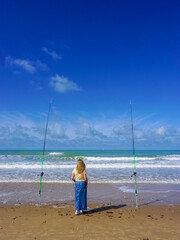 A lonely woman contemplates the sea between two fishing rods, on a beautiful day of sun and sea