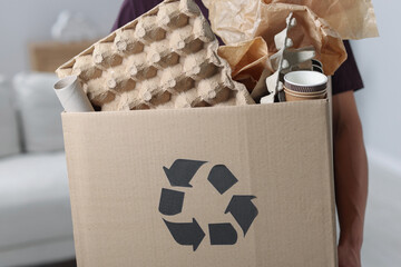 Recycling. Man holding cardboard box with different waste paper indoors, closeup