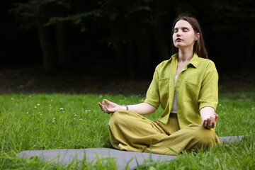 Woman meditating in lotus pose to heal or restore her aura in park, space for text