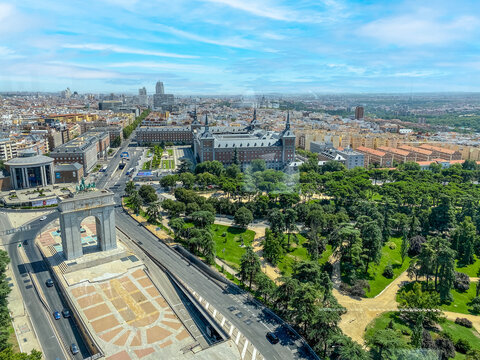 Parque del Oeste and the Arco de la Victoria stand majestically in this panoramic view of Madrid. The scene captures the vibrant mix of urban nature, monumental architecture, and everyday city life