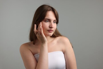 Fototapeta premium Beautiful woman applying cream onto her face on gray background