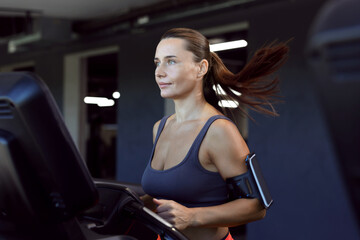 Fototapeta premium Athletic woman with armband training on treadmill in gym