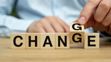 A person's hand is turning a wooden block to change the word 'CHANGE' to 'CHANGE' by flipping the letter 'G' to 'E'.