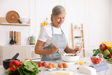 Senior woman cooking salad at white marble table in kitchen