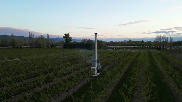 Frost protection fan in agricultural field at cold morning sunrise, anti frost wind machine in orchard to protect crops from freezing temperatures in spring