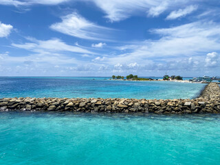 Fototapeta premium Rocky Breakwater and Vibrant Turquoise Water with Boats and Islands ocean blue