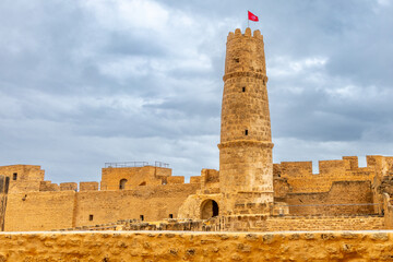 Inner yards and watch tower with tunisian flag on the top of Ribat of Monastir under cloudy skies, Monastir, Monastir Governorate, Tunisia