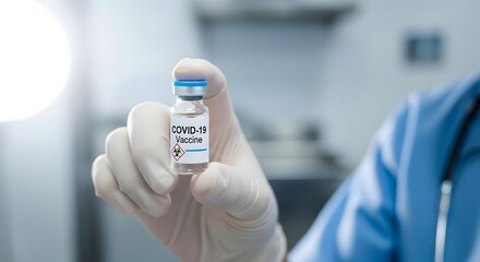 Close up of a gloved hand holding a vial of covid 19 vaccine in a medical setting with a doctor or nurse in the background