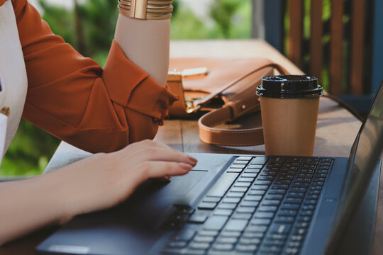 Young blonde business woman is engaged in remote work at a street-side table, using her laptop while sipping coffee and soaking in the atmosphere.