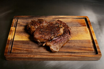 Grilled beef steak resting on wooden cutting board, seasoned and cooked with seared crust