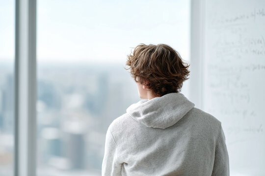 Contemplative man gazes out a large window. Back view.  Modern, bright workspace. Thinking, future concepts, strategy, and innovation. Ideal for business.