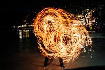 Fire dancer performing with flames at night on the beach