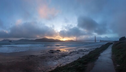 Obraz premium The image shows a landscape view of the Golden Gate Bridge from a beach at sunset, with waves and clouds present in the scene.