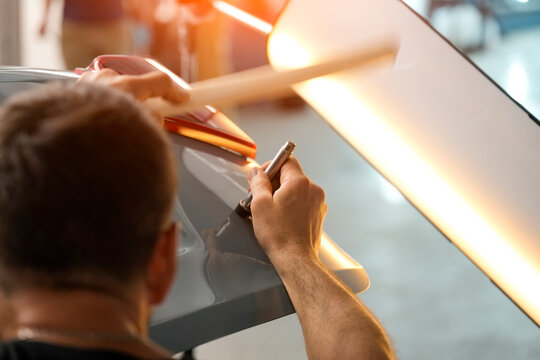 Wooden brace and light are used. Inside a Garage, an automotive technician is shown from the shoulders up using a specialized tool to repair a dent on a gray automobile - Powered by Adobe