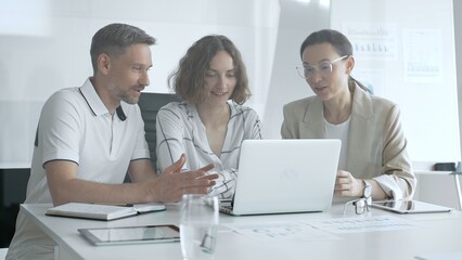 Business professionals reviewing marketing analytics on laptops, working together strategically in contemporary workplace with minimalist interior design and collaborative atmosphere